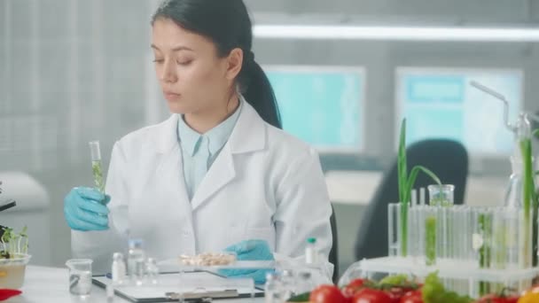 亚洲女性研究人员将液体注入带有绿色幼苗的试管，并做笔记。微生物学家分析产品的质量。绿芽的研究、基因改造图片