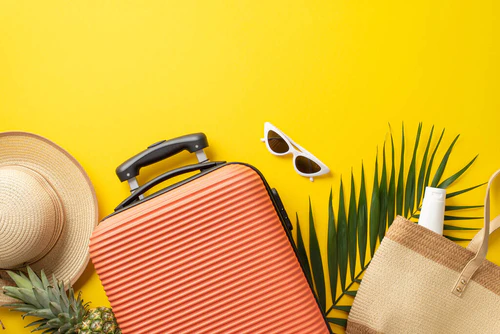 热带度假的概念。顶部照片橙色行李箱周围有草帽和草袋，棕榈叶和太阳镜孤立明亮的黄色背景与复制空间图片