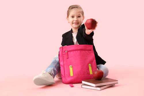 带着背包、书和苹果的粉红背景的小女孩图片