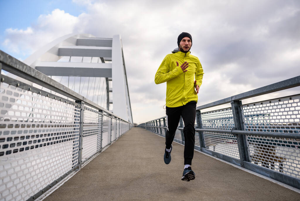 迷人的健康男人沿着现代的大桥跑得快。采购产品运动，慢跑，运动，冬天。男子运动员跑步.图片