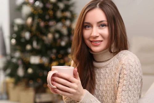 美丽的年轻的微笑的女人，在圣诞树旁喝茶，文字的空间图片