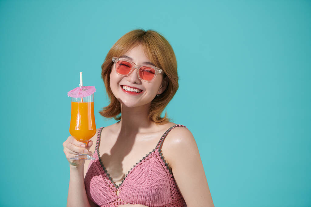 健康微笑的女人拿着一杯橙汁，与绿松石背景隔离